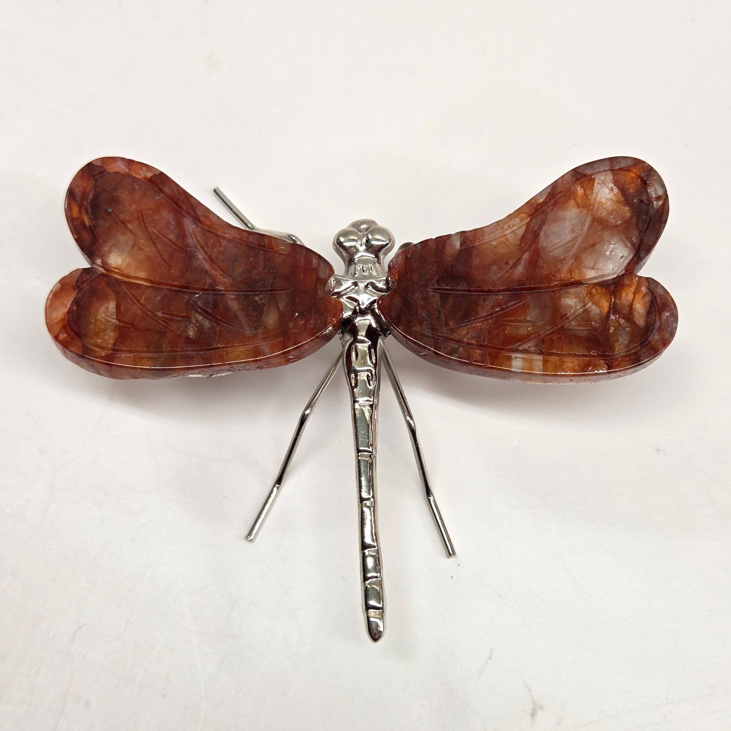 Dragonfly shaped carving with Fire Quartz crystal wings and a silver body on a white background