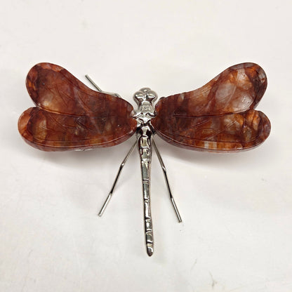 Dragonfly shaped carving with Fire Quartz crystal wings and a silver body on a white background