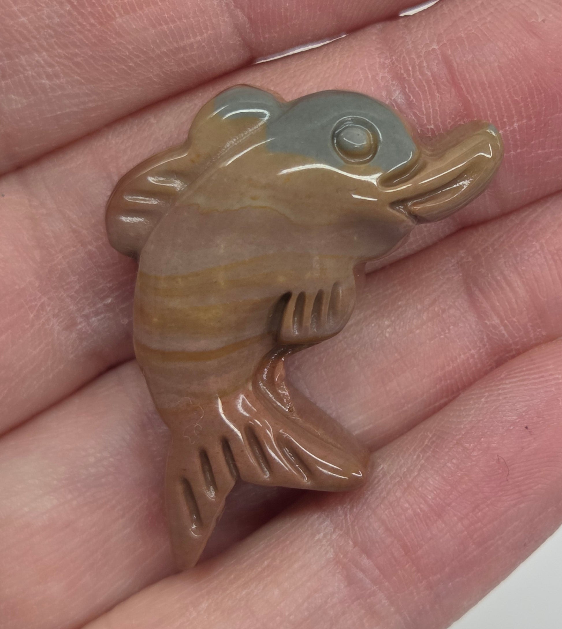 Hand holding a mini Alashan Agate multi-colored dolphin carving on a white background