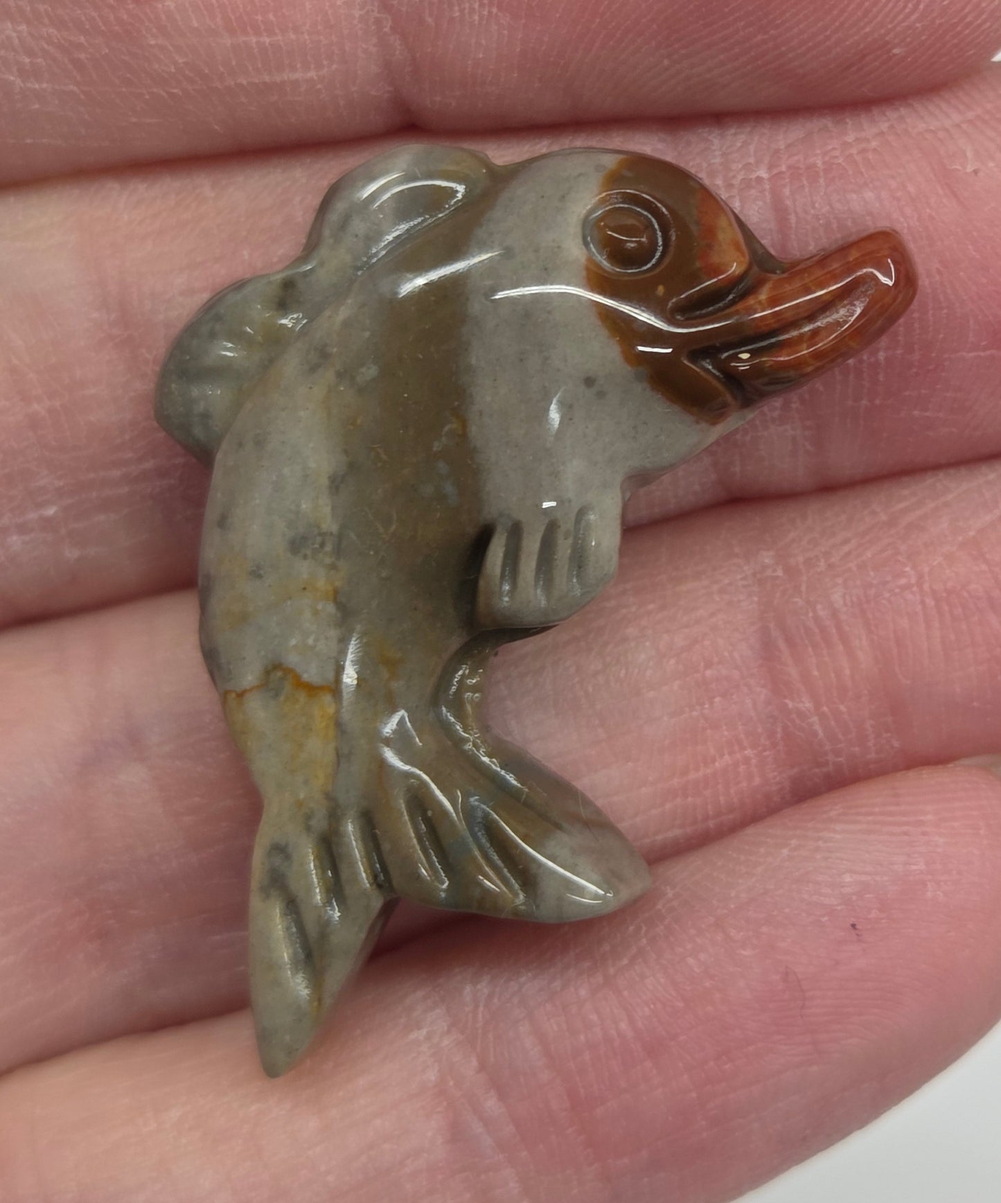 Hand holding a mini Alashan Agate multi-colored dolphin carving on a white background