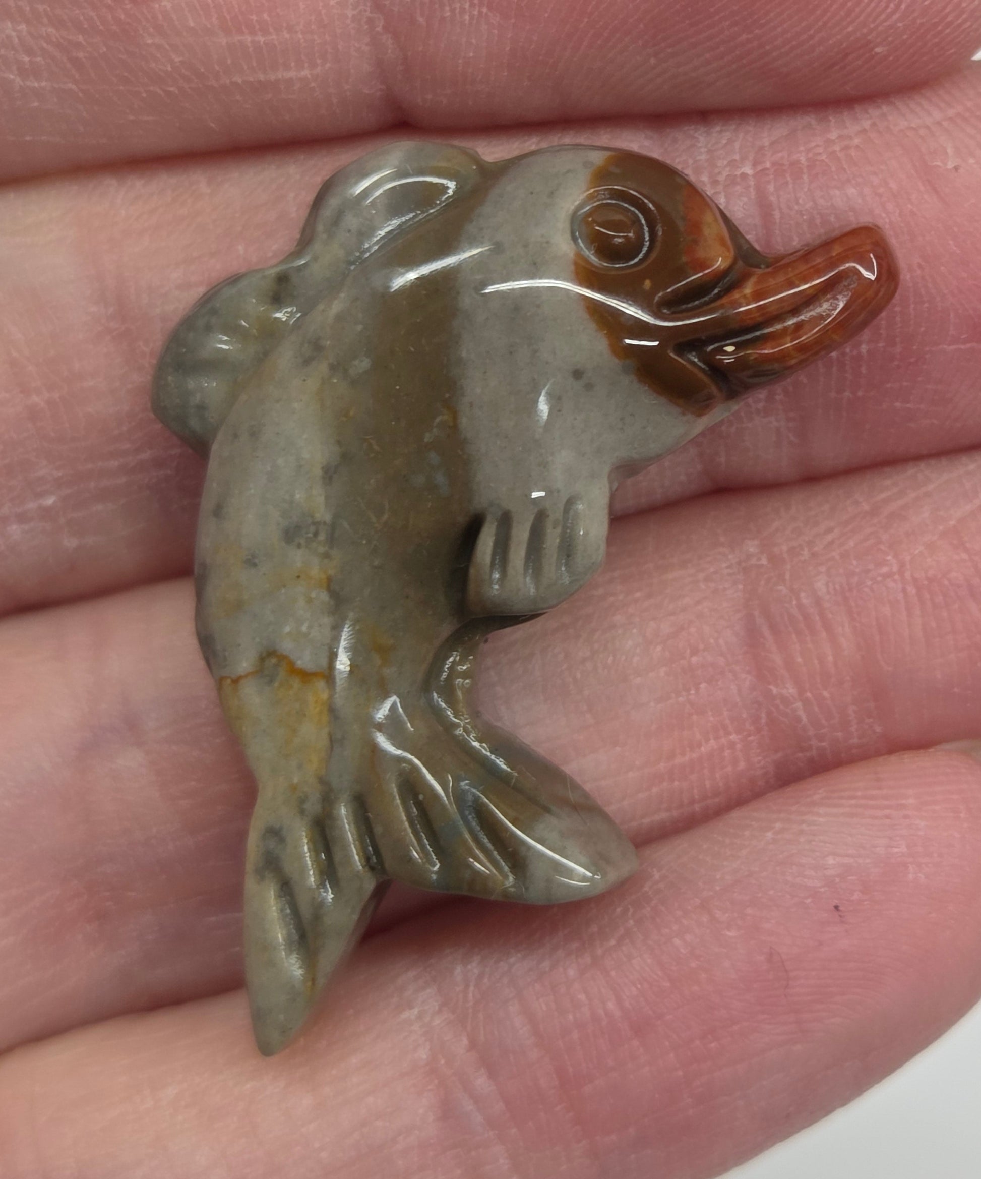 Hand holding a mini Alashan Agate multi-colored dolphin carving on a white background