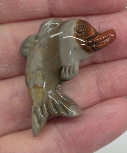 Hand holding a mini Alashan Agate multi-colored dolphin carving on a white background