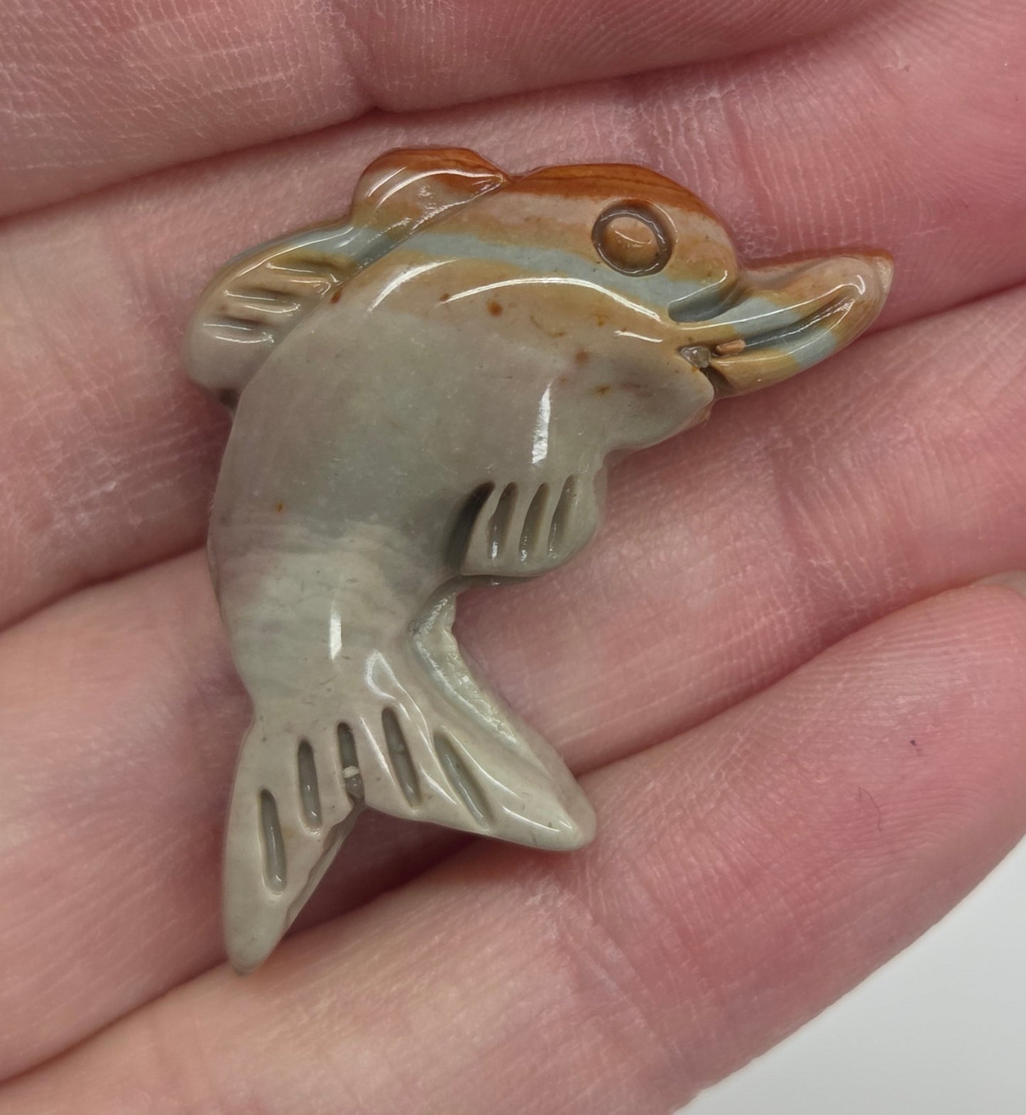 Hand holding a mini Alashan Agate multi-colored dolphin carving on a white background