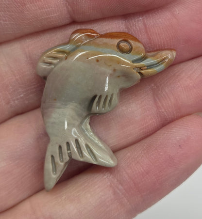 Hand holding a mini Alashan Agate multi-colored dolphin carving on a white background