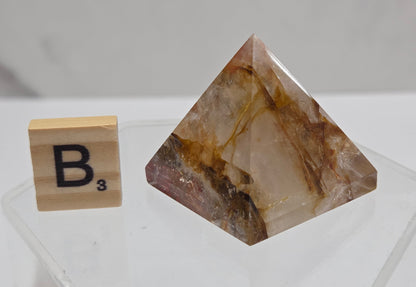 Pyramidal crystal on a clear stand with a wooden block labeled 'B' on a white background