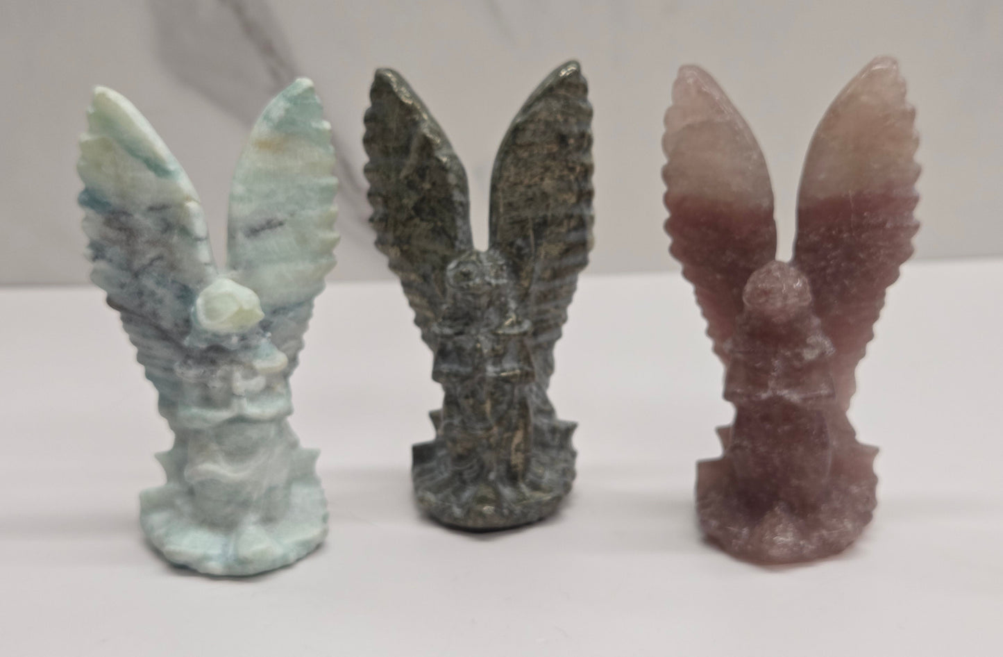 Three stone angel crystal sculptures on a white surface with a neutral background