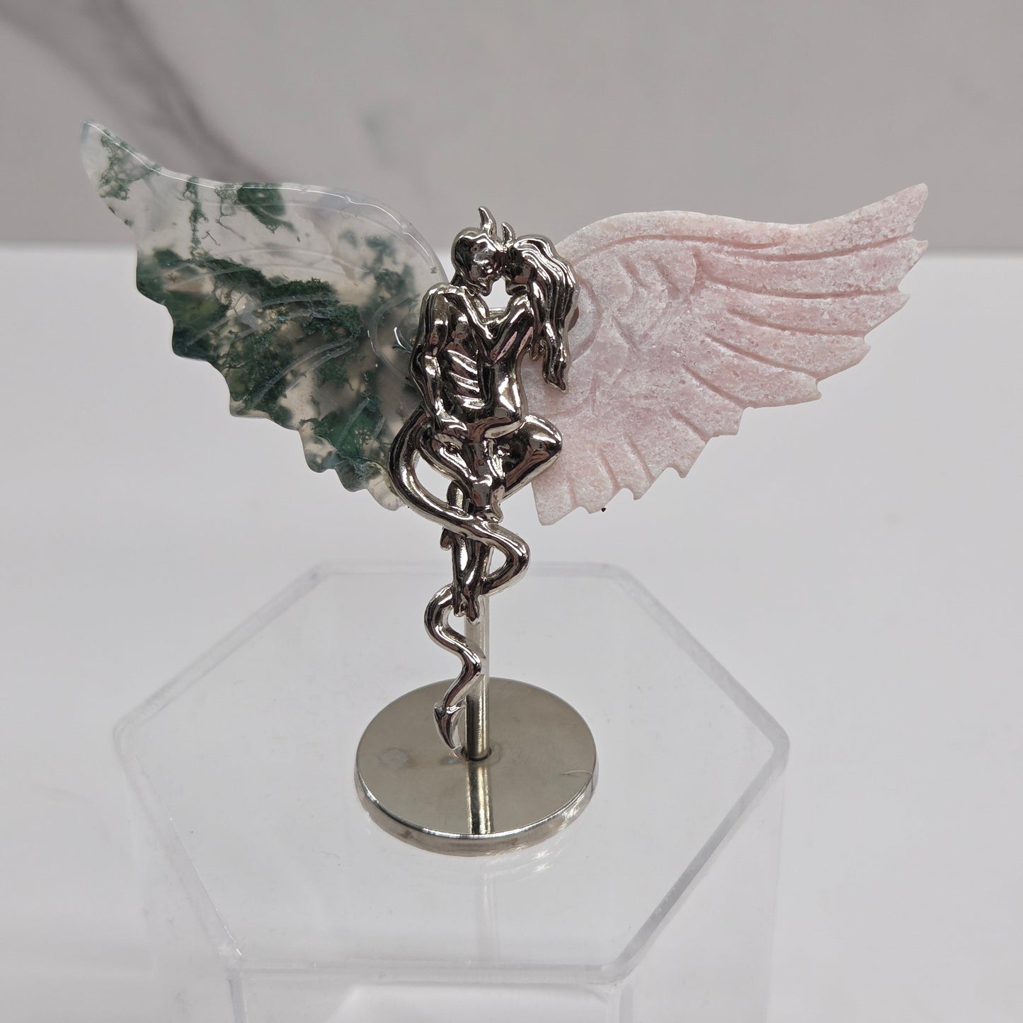 Carved Moss Agate and Pink Opal crystal wings on a silver devil and harpy stand against a white background
