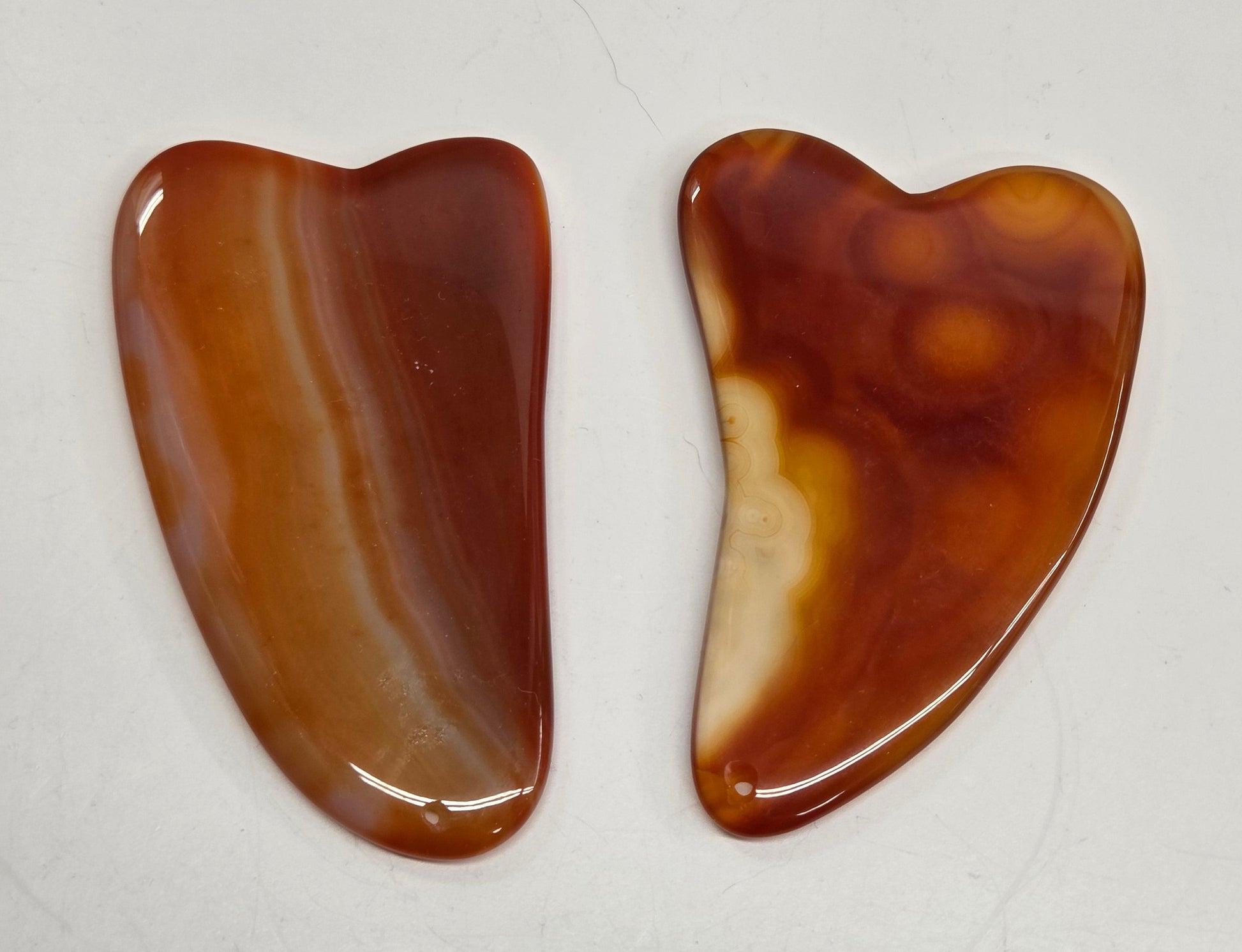 Two Carnelian gua sha tools on a white background