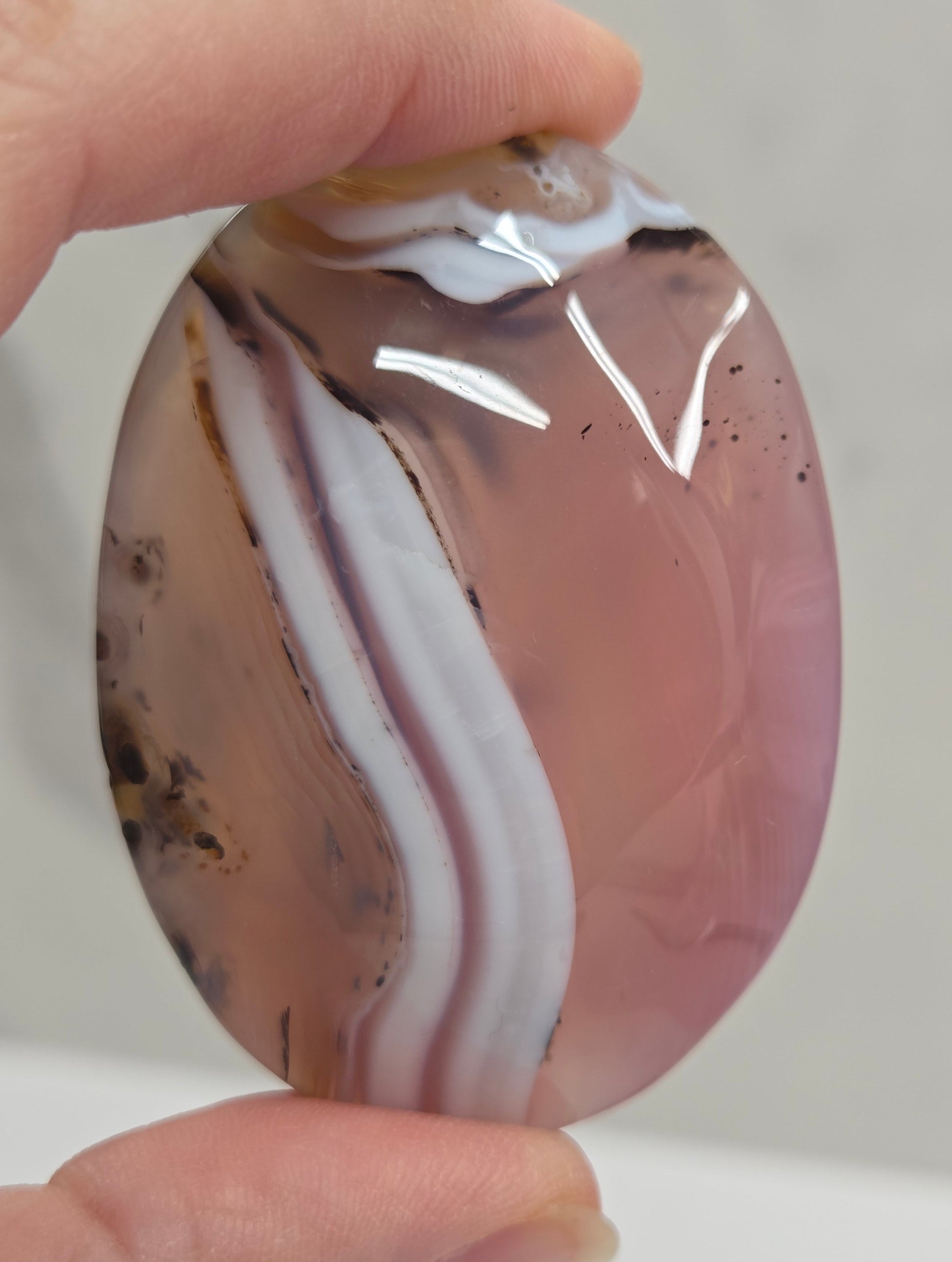 Hand holding a marbled stone with brown, white, and black patterns on a plain background