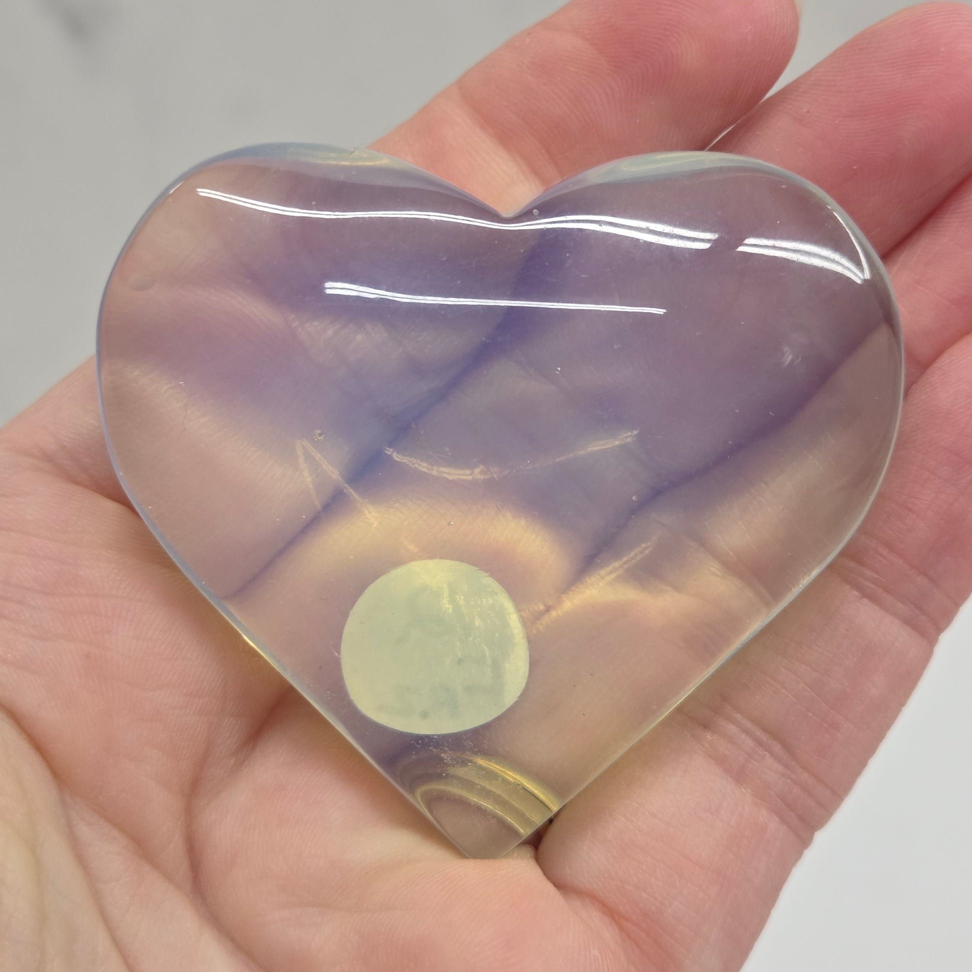 Heart-shaped object with a gradient of purple and yellow held in a hand against a neutral background