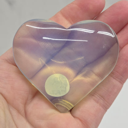 Heart-shaped object with a gradient of purple and yellow held in a hand against a neutral background