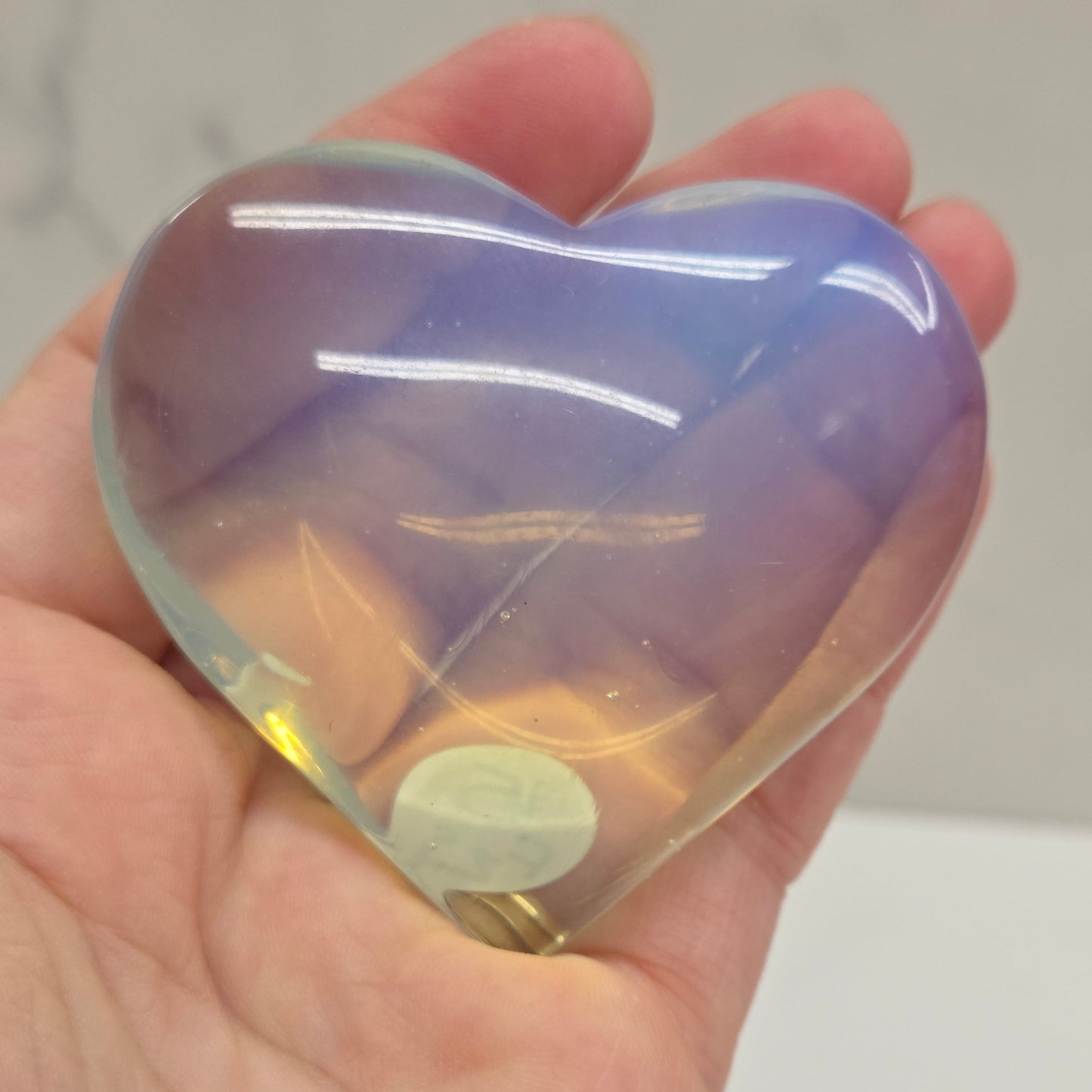 Heart-shaped object with a gradient of purple and yellow held in a hand against a neutral background