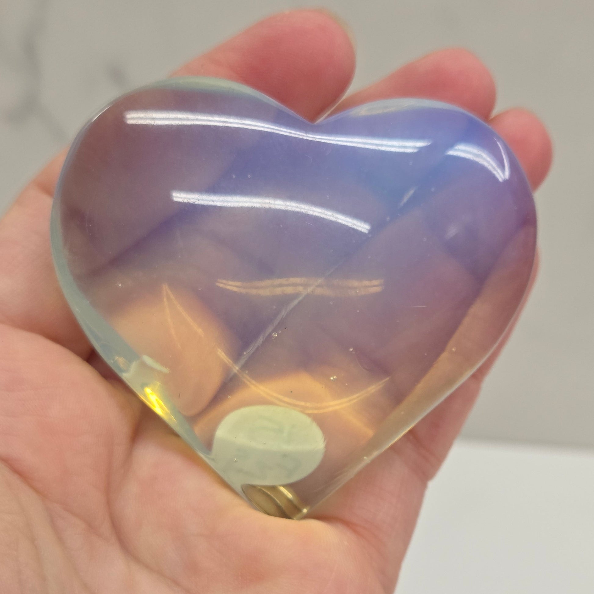 Heart-shaped object with a gradient of purple and yellow held in a hand against a neutral background