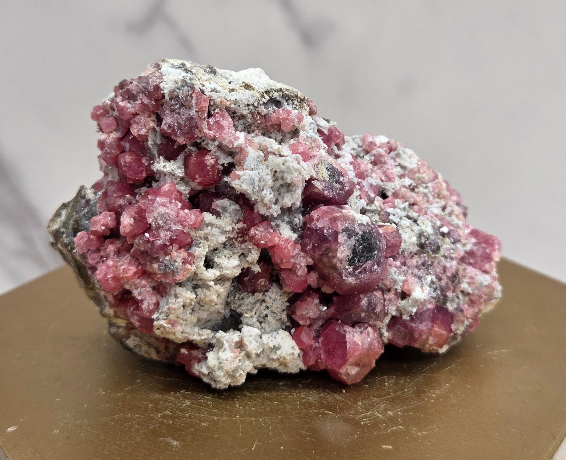 Pink and white mineral specimen on a hexagonal base with a marble-patterned wall in the background