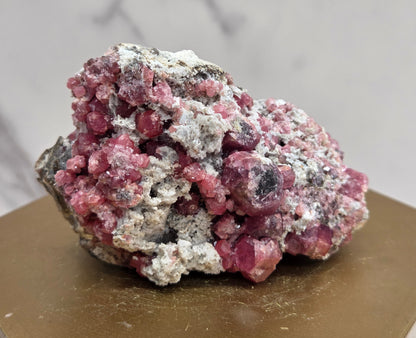 Pink and white mineral specimen on a hexagonal base with a marble-patterned wall in the background