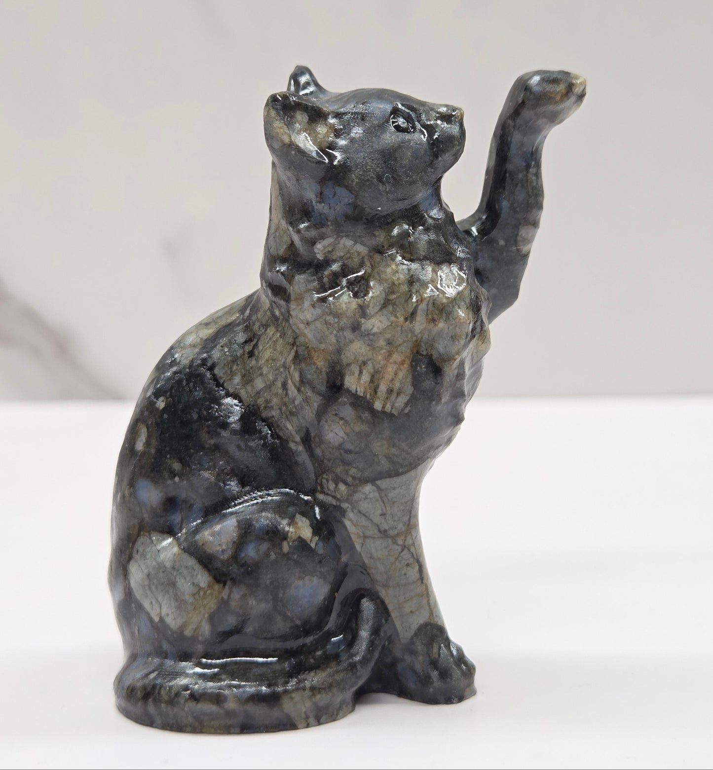 Cat crystal figurine made of  Que Sera, with tan, black and blue on a white surface with a light gray background
