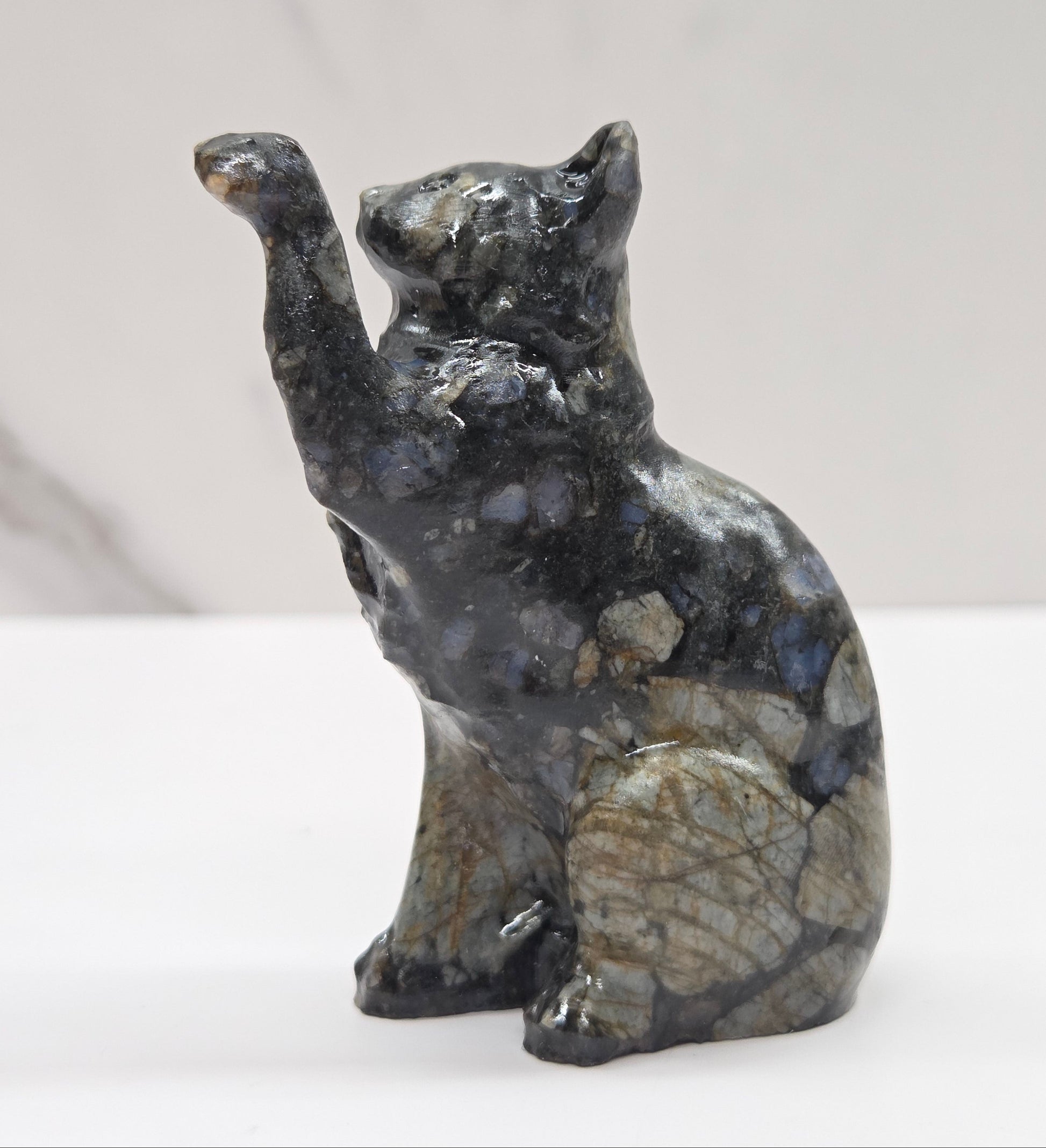 Cat crystal figurine made of  Que Sera, with tan, black and blue on a white surface with a light gray background
