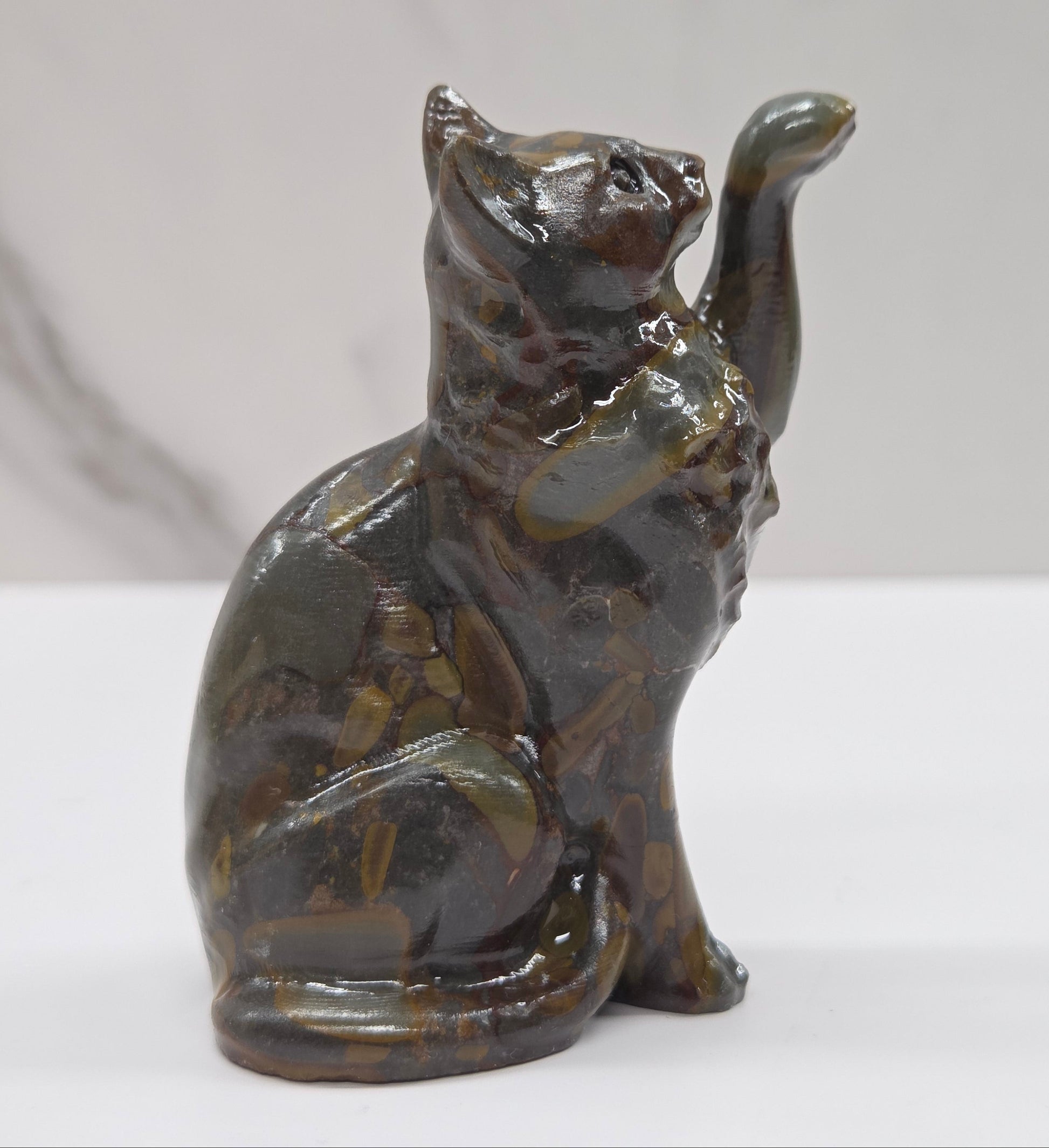 Cat crystal figurine made of  Bamboo Jasper, with banding of tan, black, brown and yellow on a white surface with a light gray background