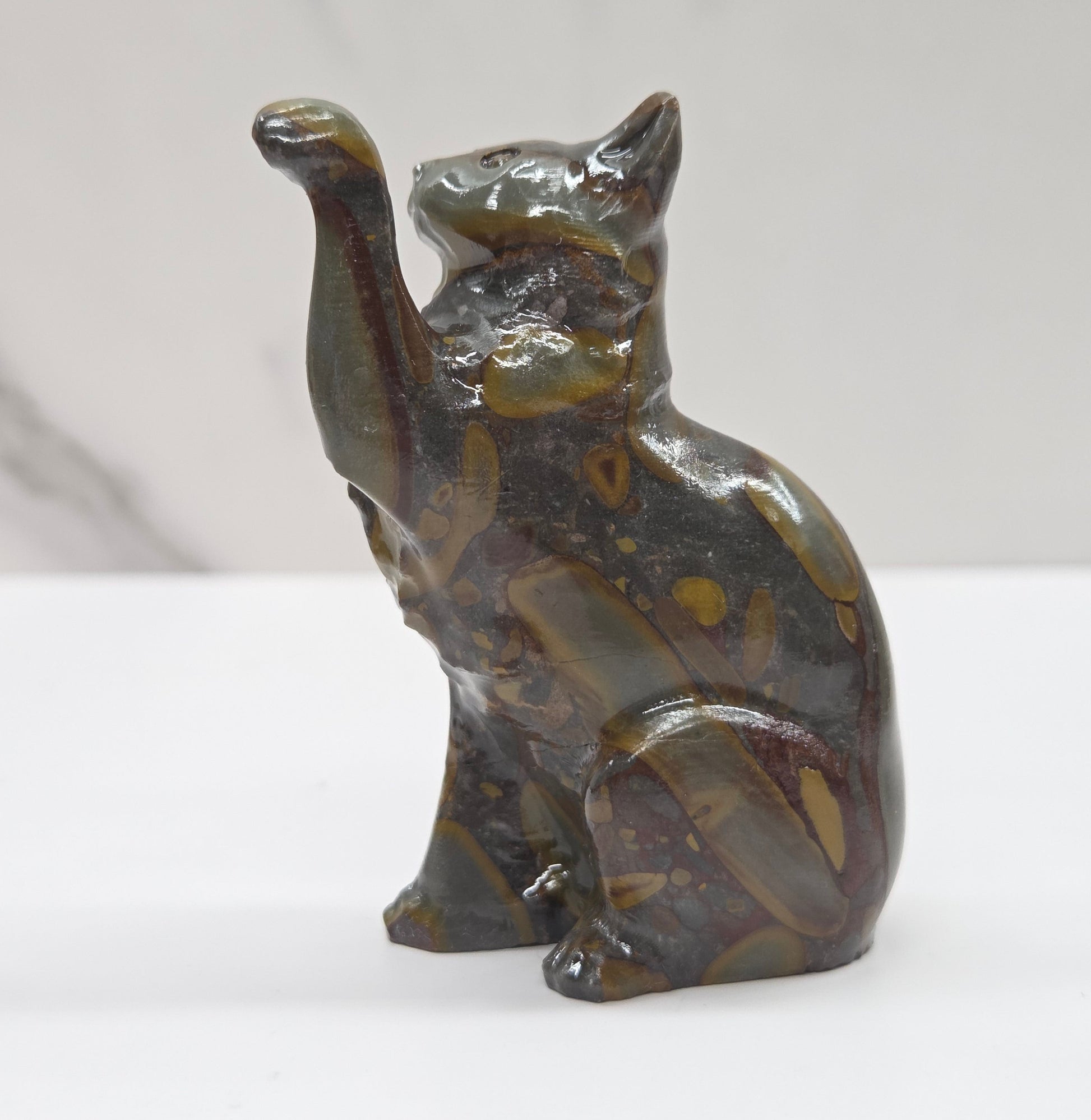 Cat crystal figurine made of  Bamboo Jasper, with banding of tan, black, brown and yellow on a white surface with a light gray background