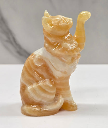 Cat crystal figurine made of  Orange Calcite, with banding of orange & white on a white surface with a light gray background