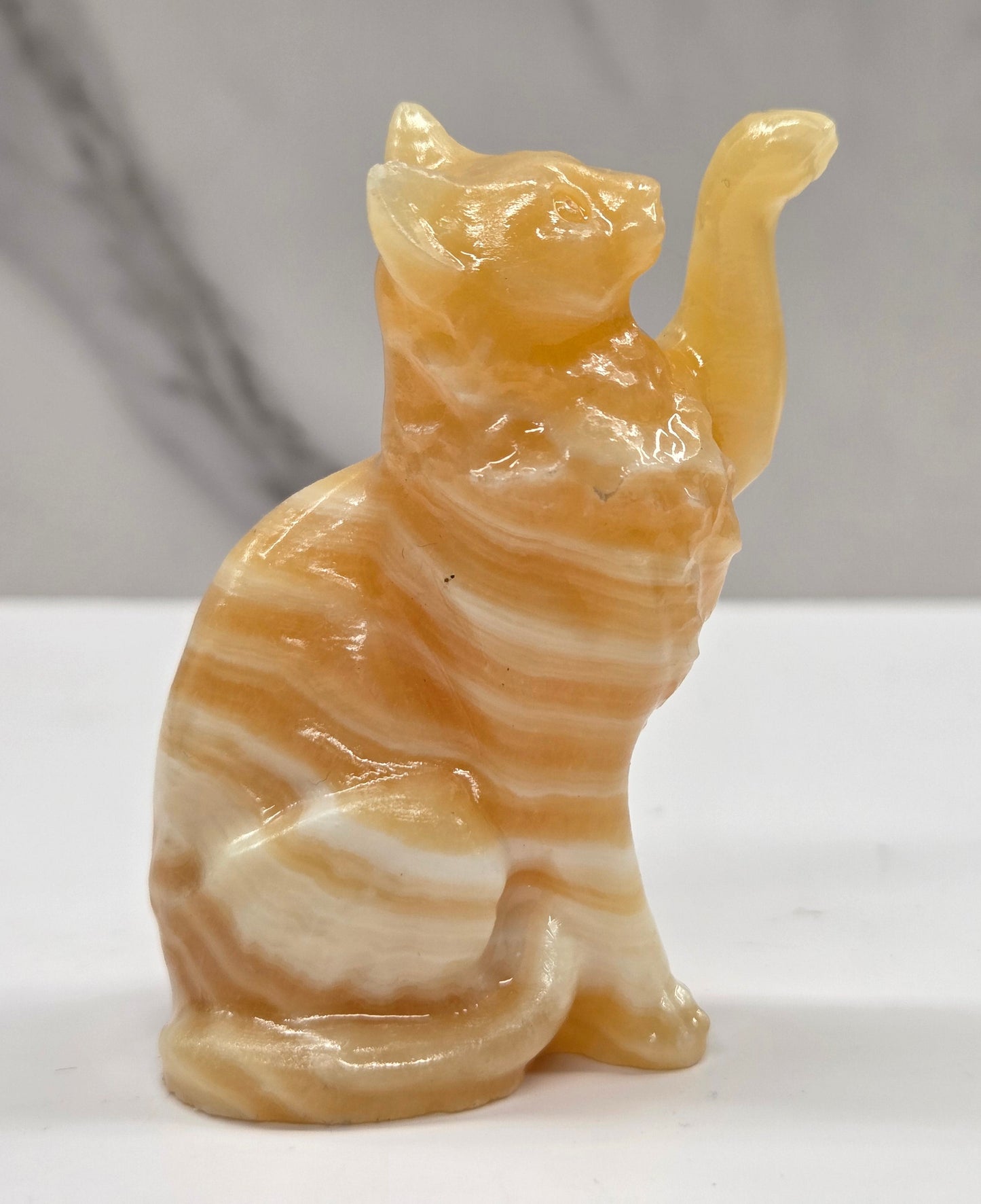 Cat crystal figurine made of  Orange Calcite, with banding of orange & white on a white surface with a light gray background