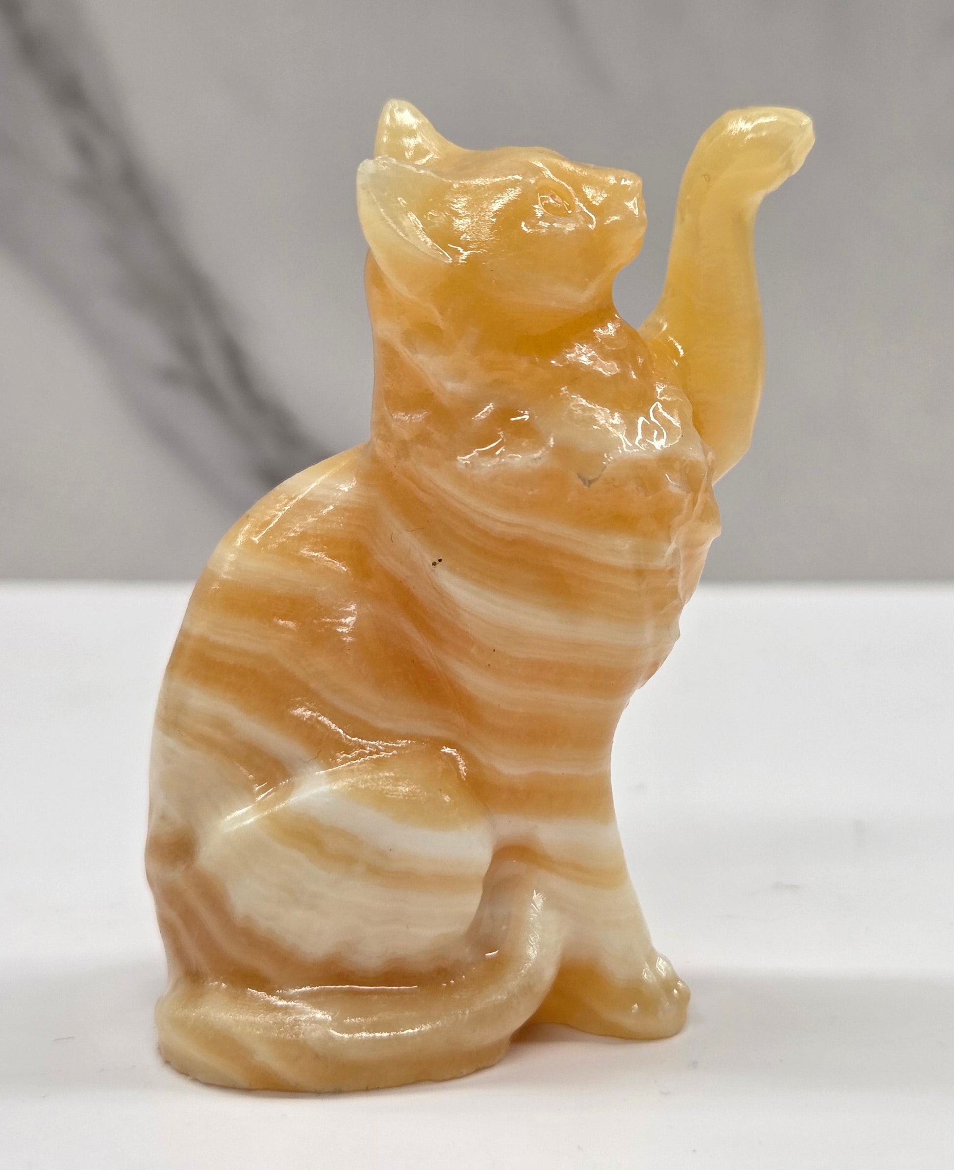 Cat crystal figurine made of  Orange Calcite, with banding of orange & white on a white surface with a light gray background