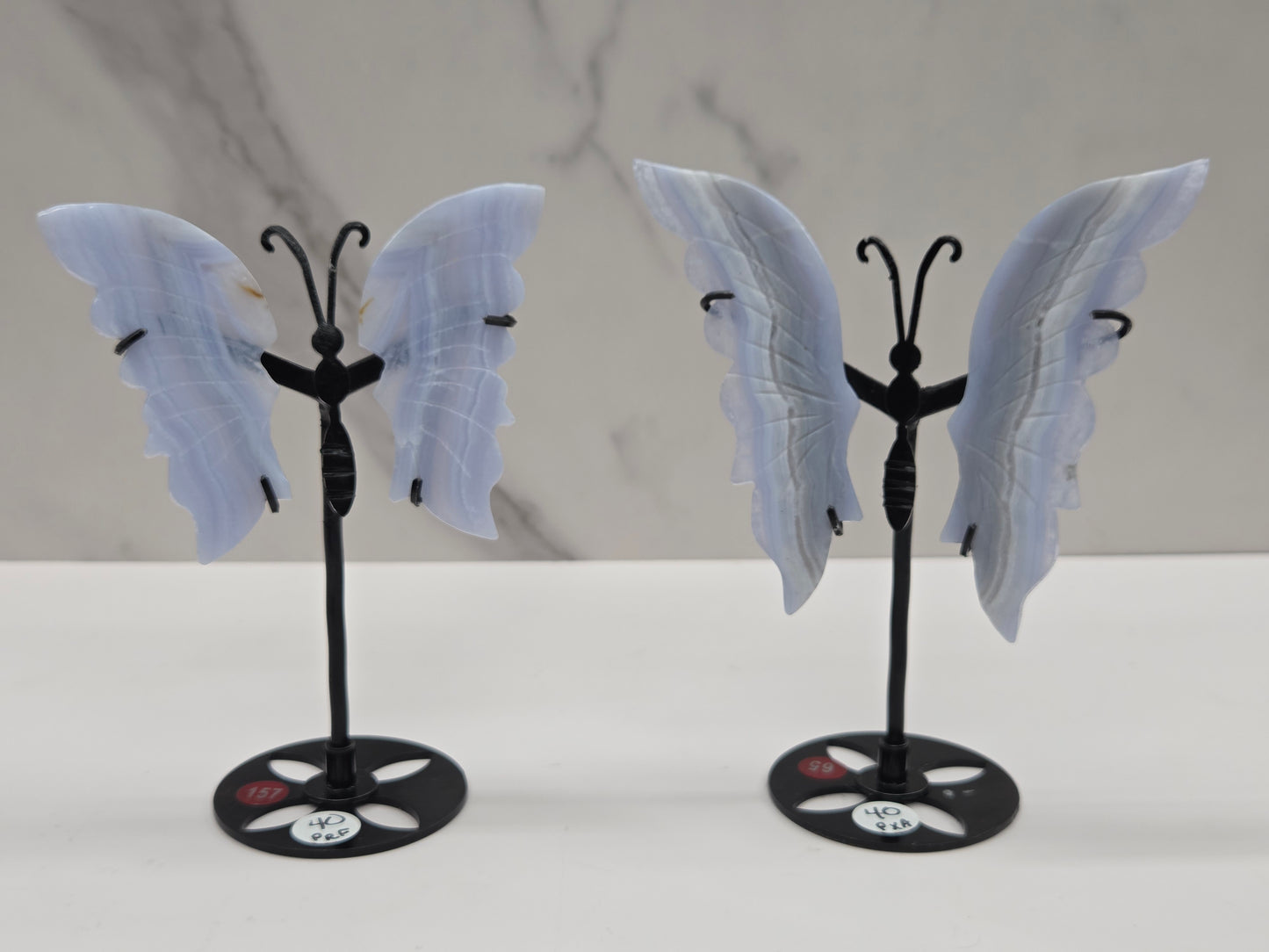 Two Blue Lace Agate butterfly figurines on stands with light blue wings and black bodies against a neutral background.