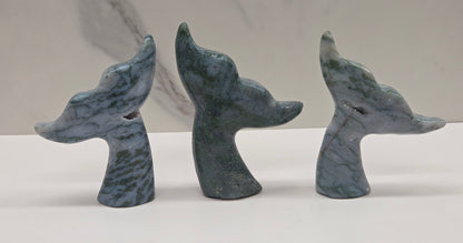 Three stone carvings of stylized whale tales, green, blues and greys and drusy crystal caves