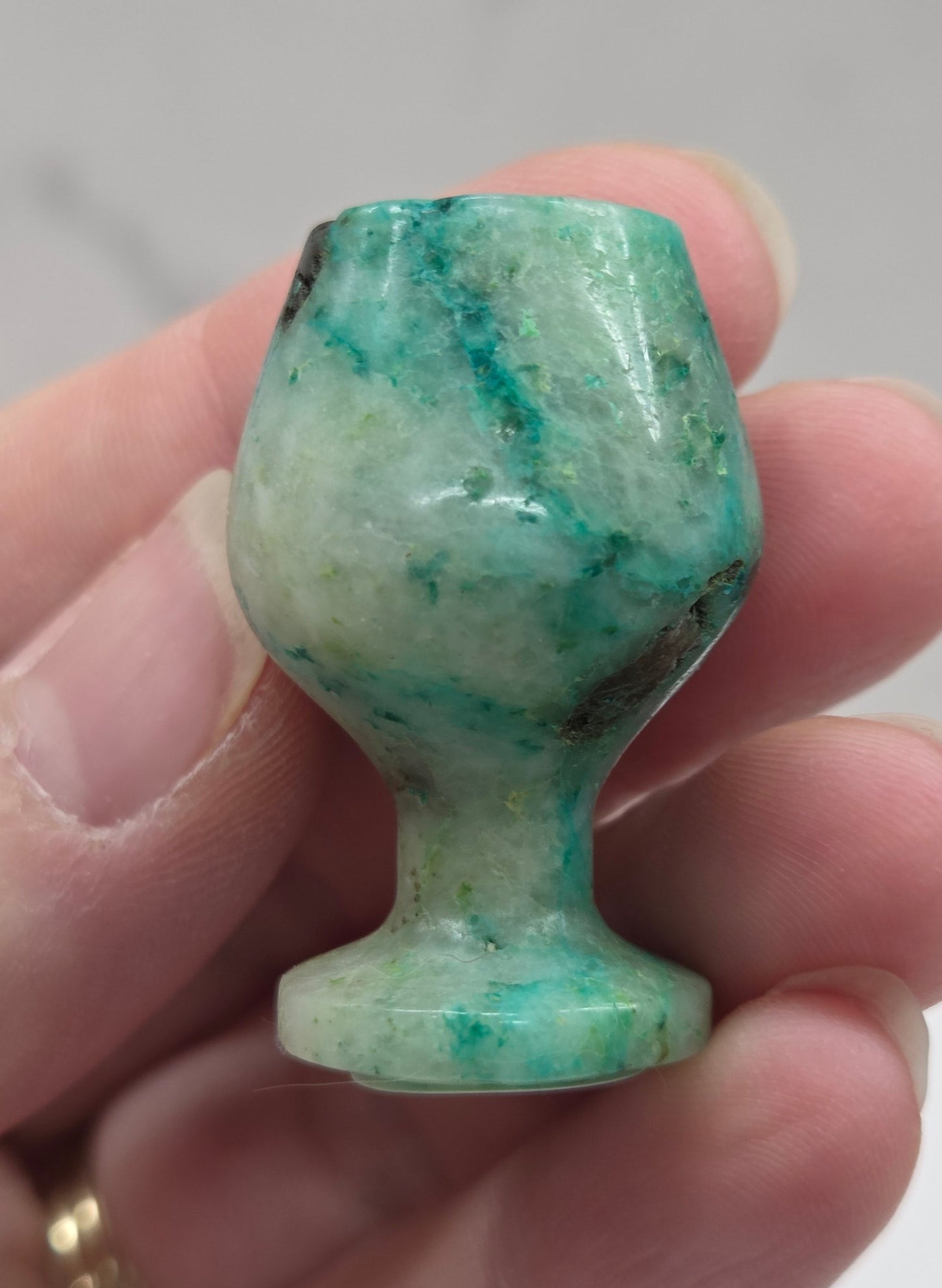 Hand holding a green stone goblet  against a neutral background