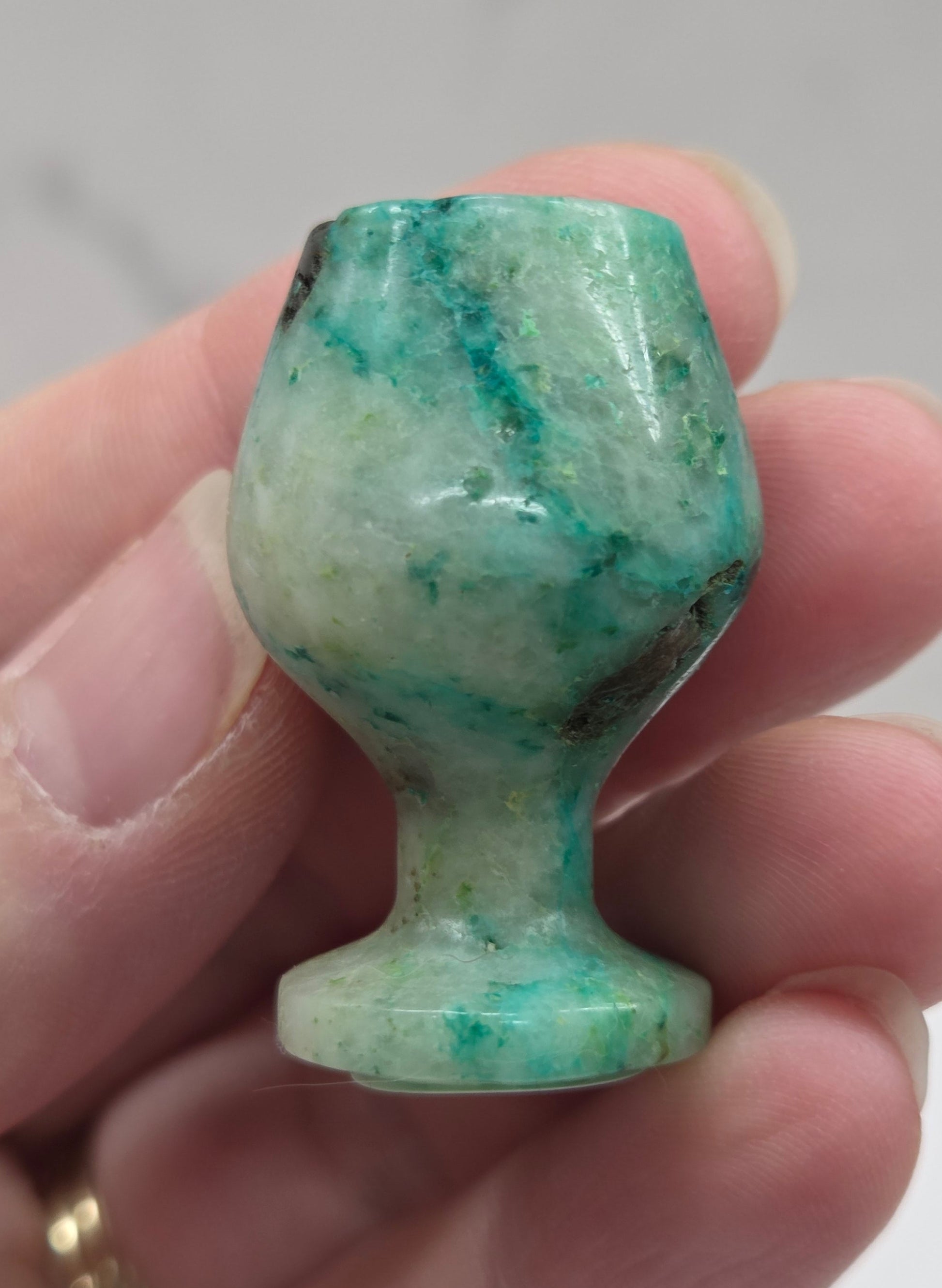 Hand holding a green stone goblet  against a neutral background