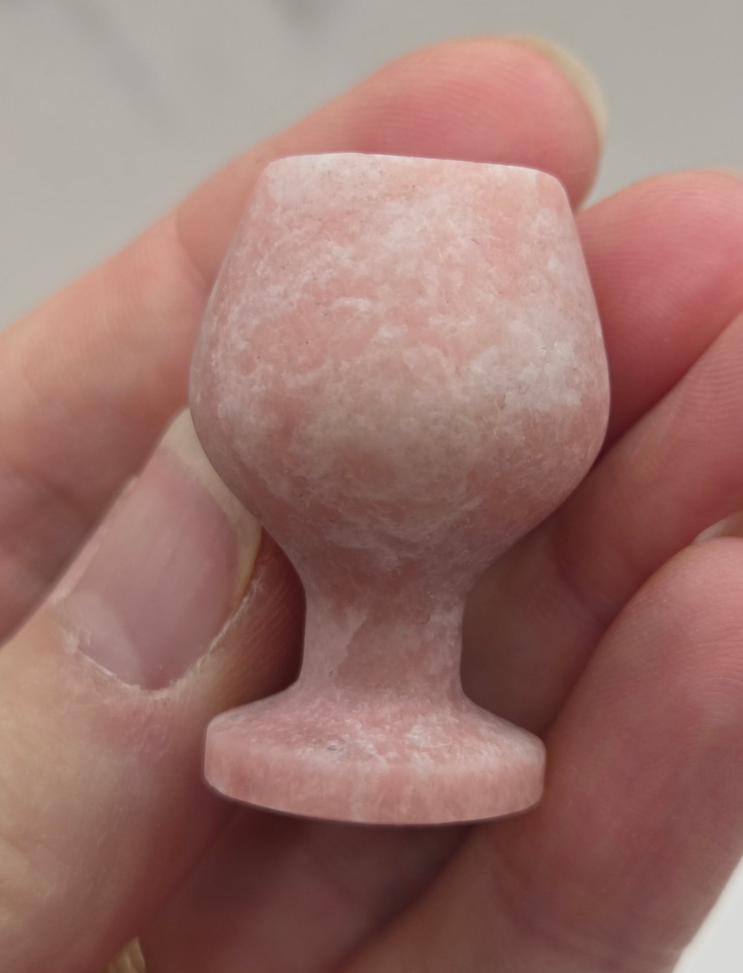 Hand holding a pink stone goblet against a neutral background