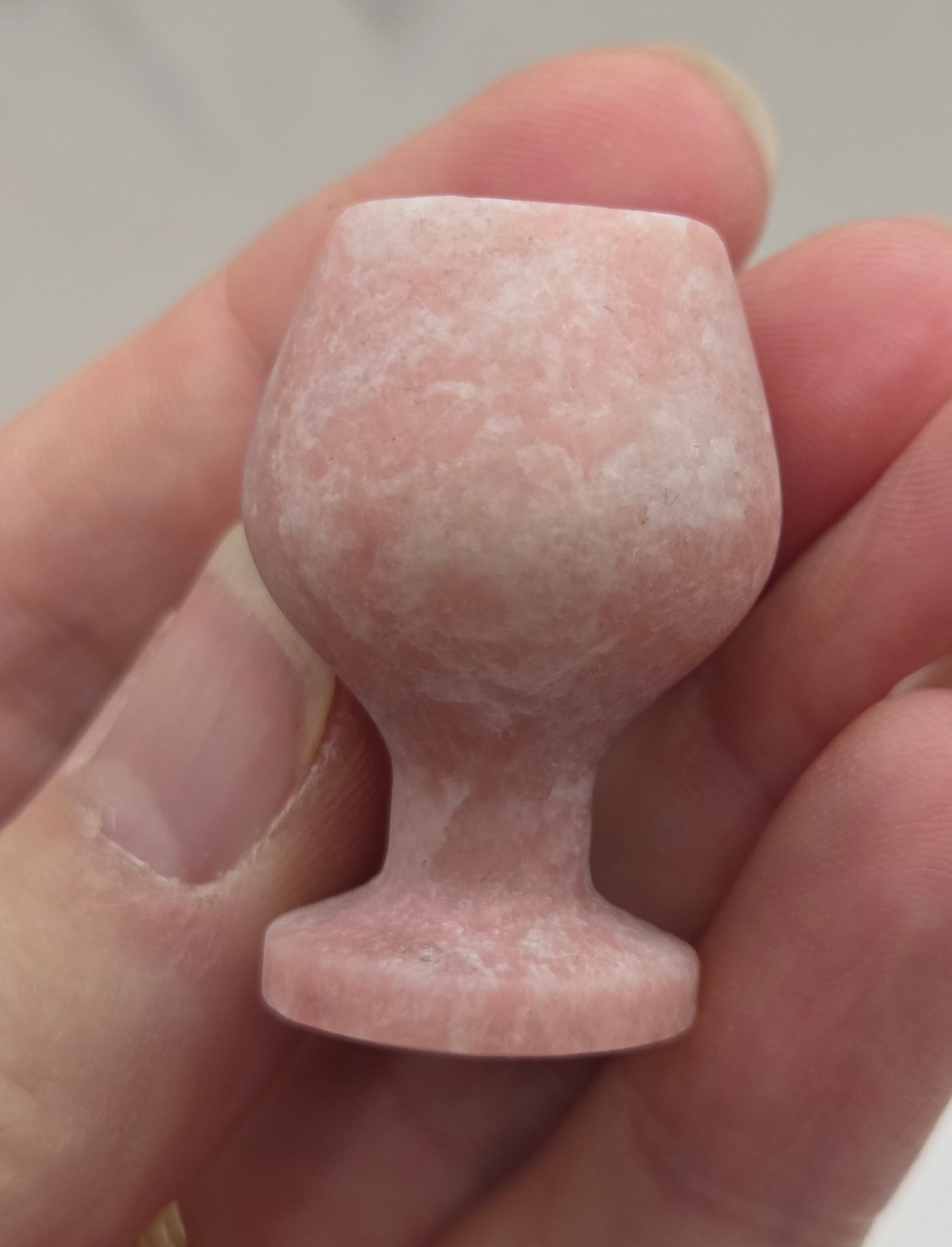 Hand holding a pink stone goblet against a neutral background
