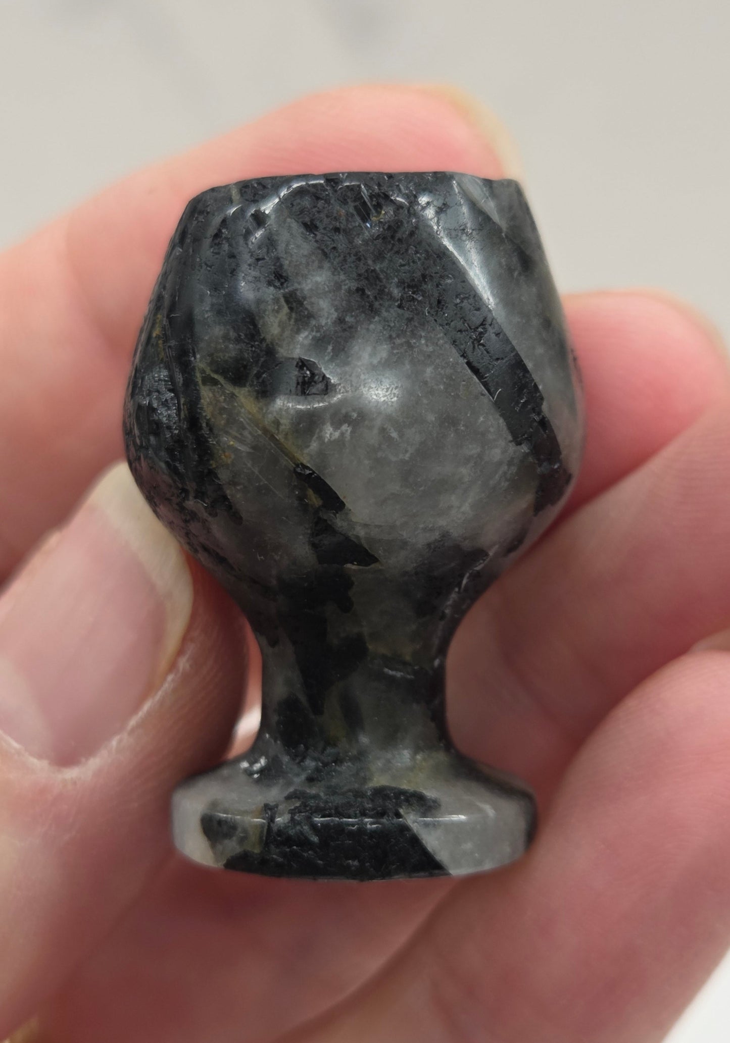 Hand holding a rough black stone goblet against a neutral background