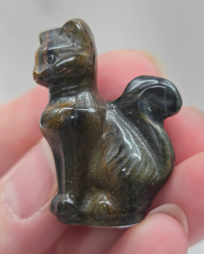 Hand holding a small Tigers Eye sculpture of a cat against a neutral background