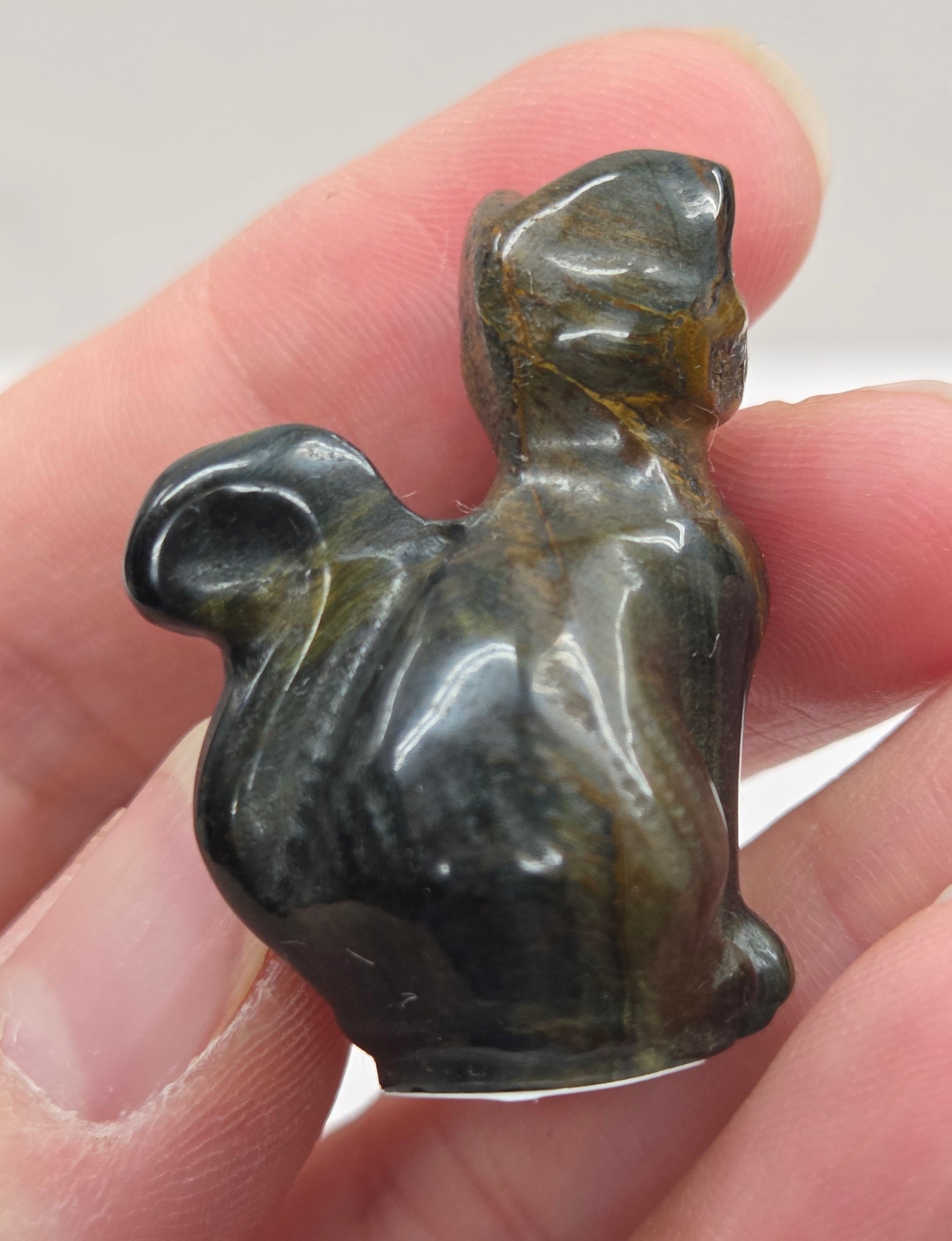 Hand holding a small Tigers Eye sculpture of a cat against a neutral background