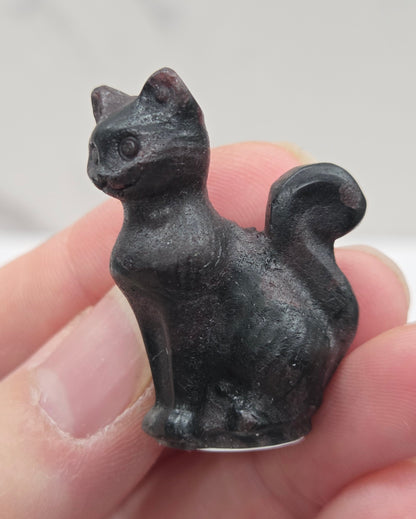Small black Garnet cat figurine held in a hand against a white background