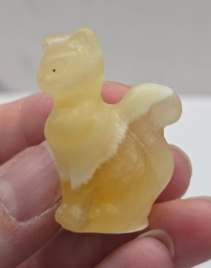 Hand holding a small Orange Calcite  sculpture of a cat against a neutral background