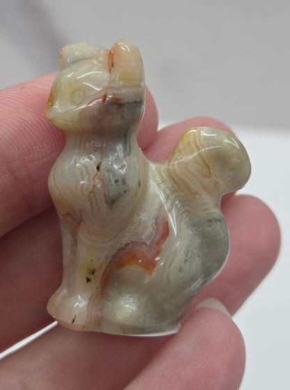 Hand holding a small Crazy Lace Agate cat sculpture with banding in yellow, tan and red