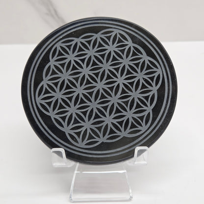 Black Obsidian circular object with geometric pattern held in a hand against a neutral background