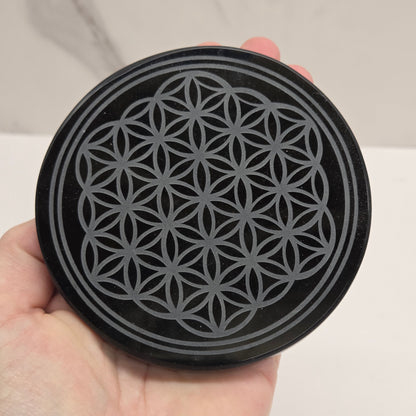 Black Obsidian circular object with geometric pattern held in a hand against a neutral background