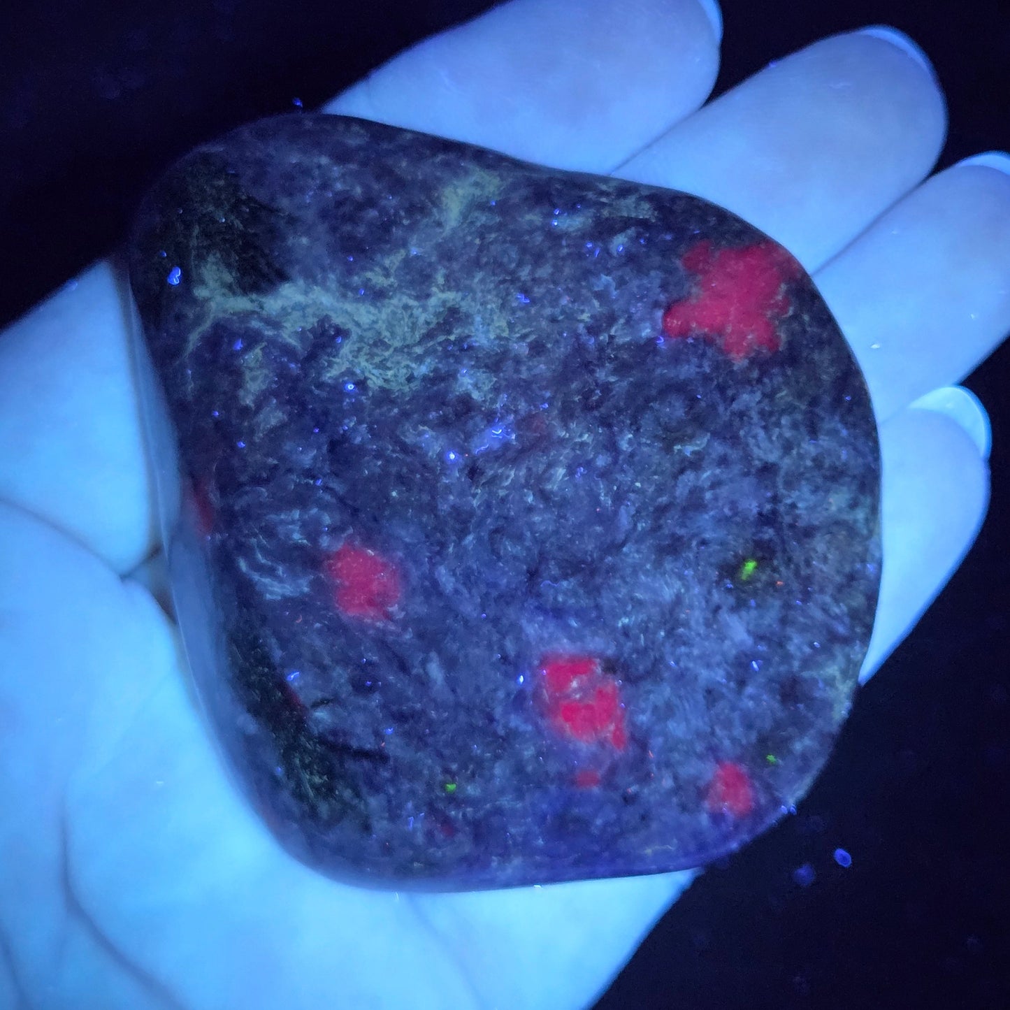 Hand holding a dark stone with red and green markings under a black light