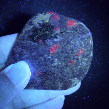 Hand holding a dark stone with red and green markings under a black light