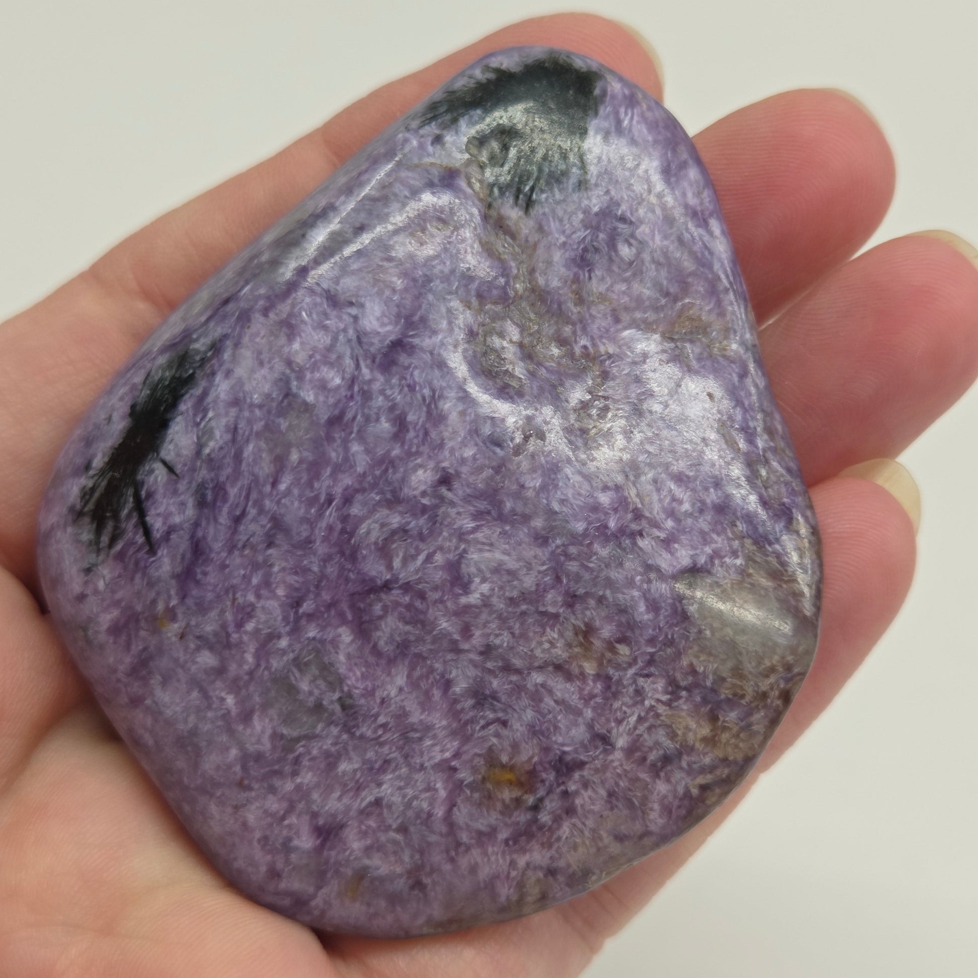 Hand holding a purple Charoite stone against a white background