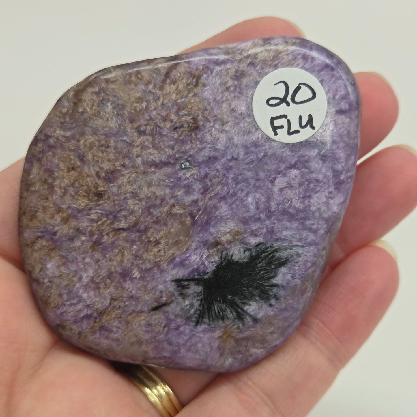 Hand holding a purple Charoite stone against a white background