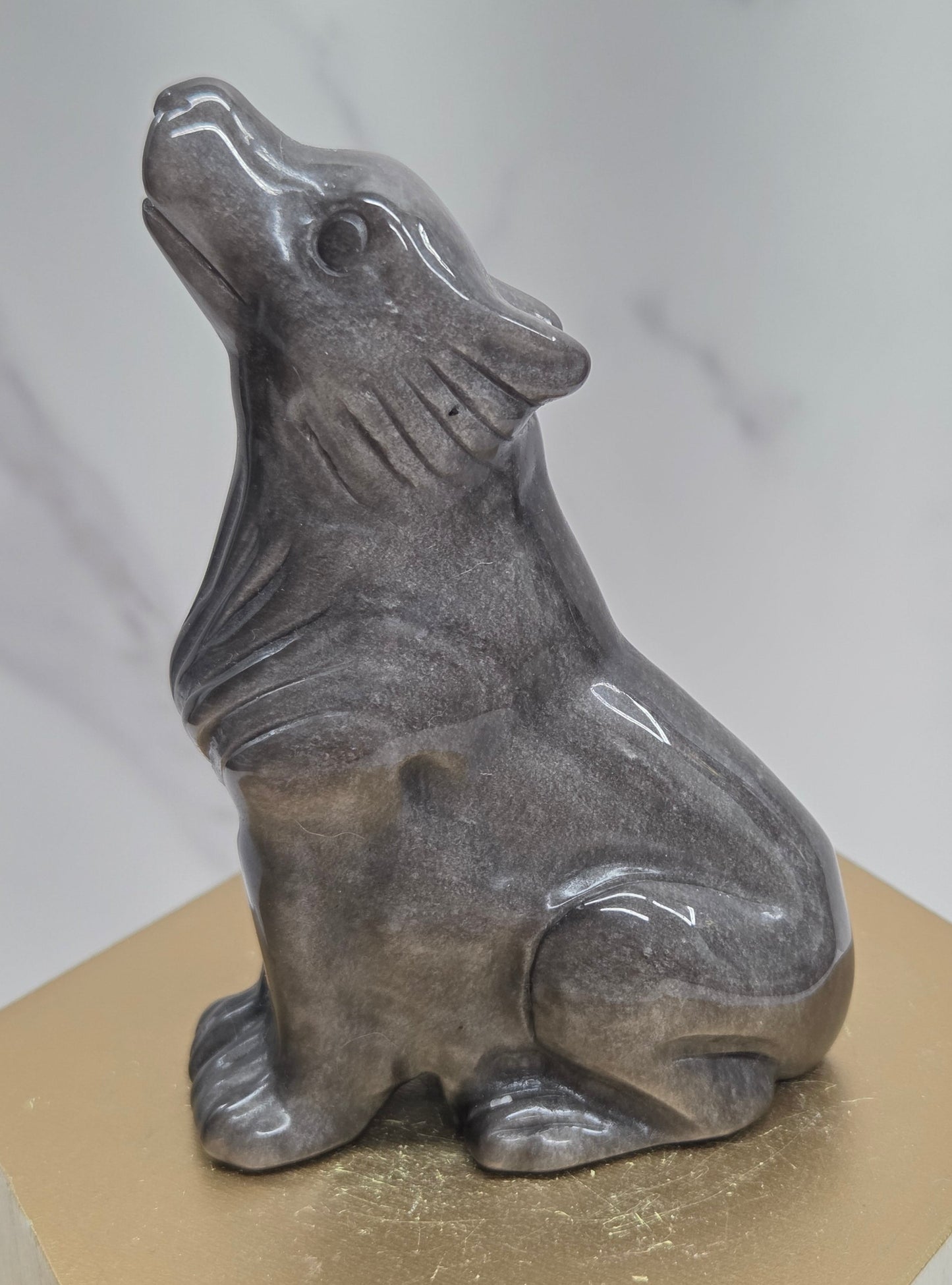 Silver sheen obsidian wolf carving on a neutral background