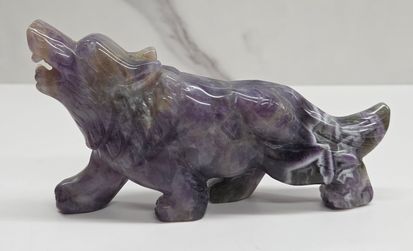 Carved Dream Amethyst figure of a wolf on a white surface with a marble-patterned wall in the background.
