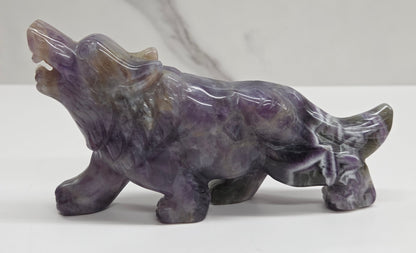 Carved Dream Amethyst figure of a wolf on a white surface with a marble-patterned wall in the background.
