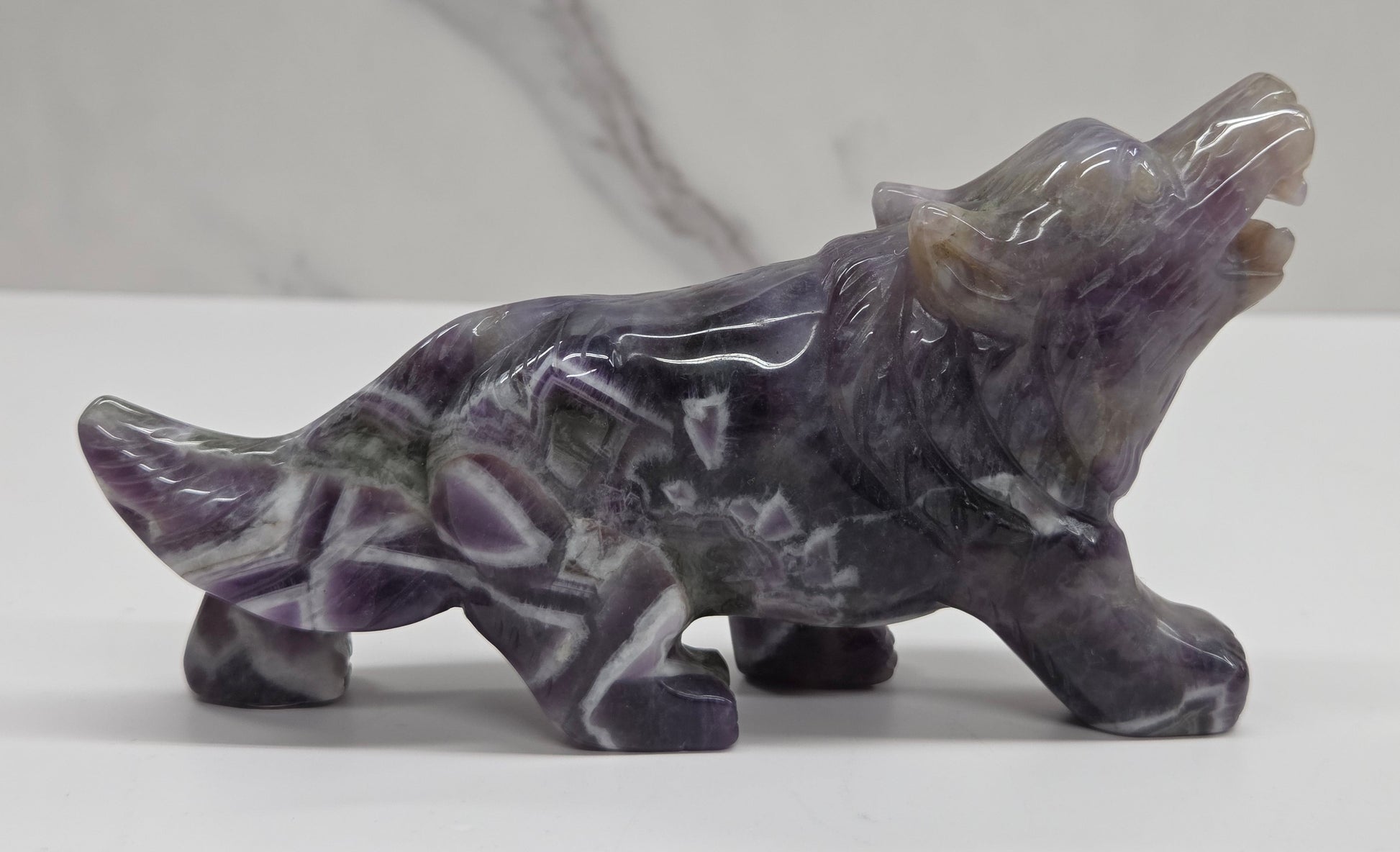 Carved Dream Amethyst figure of a wolf on a white surface with a marble-patterned wall in the background.