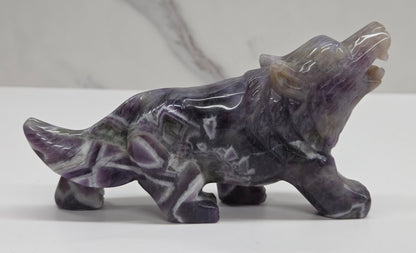 Carved Dream Amethyst figure of a wolf on a white surface with a marble-patterned wall in the background.
