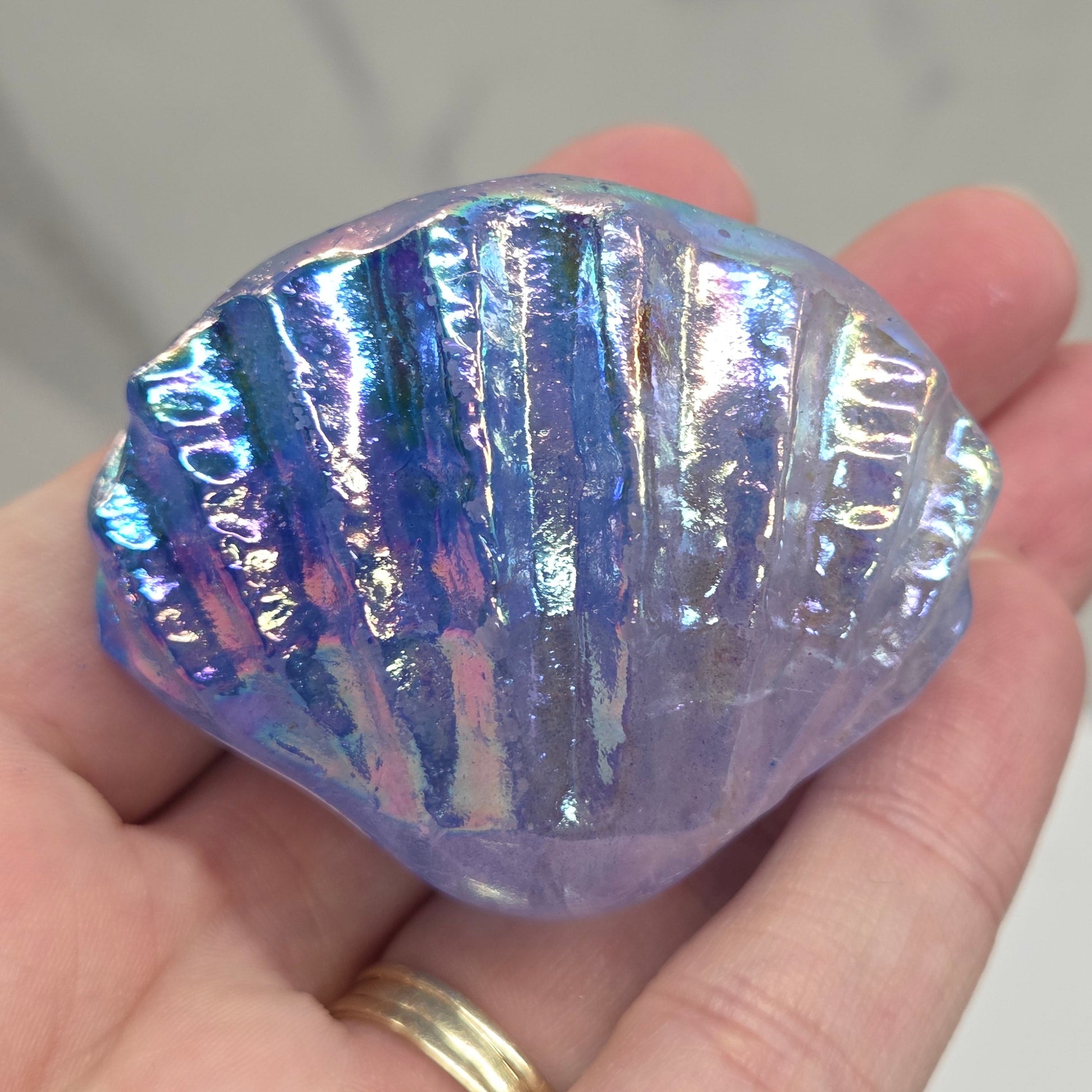 Hand holding a blue and purple iridescent crystal clam carving against a neutral background